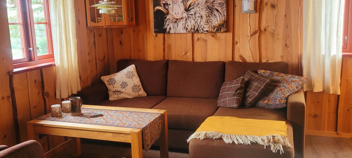 Stova i Hytte 2 med brun sofa, salongbord og villsau-bilete på veggen